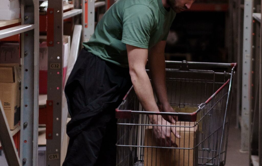 trabajador coge una caja dentro de un carrito de compra en un almacén